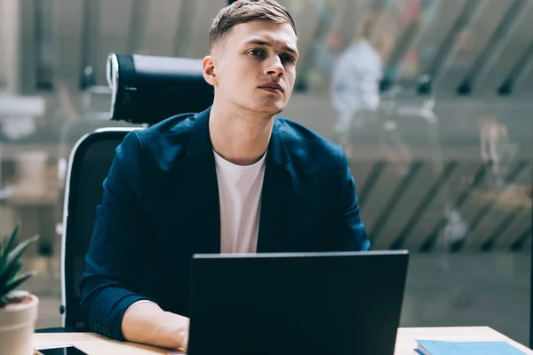 Puzzled interested focused specialist looking away during occupation on startup project on laptop at table and listening to noise outside office