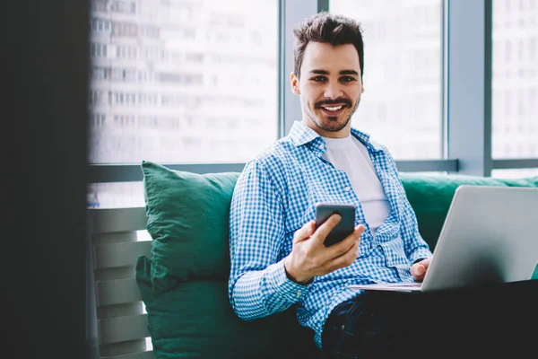 Neşeli Gülümseyen Adam Dizüstü Bilgisayarı Bacaklarının Üzerinde Partneriyle Cep Telefonu — Stok fotoğraf