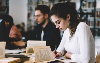 Üniversite projesinde çalışan, rahat giyinen, edebiyat okuyan, not defterinde not tutan kütüphanedeki masada oturan genç bir kadın.