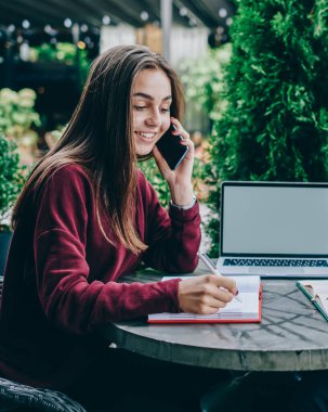 Neşeli erkek ve kadın meslektaşları cep telefonları konuşuyor ve netbook ile kafe terasında oturan bilgi notları yapma, hipsters hücresel gerçek konuşma iletişimi görmezden