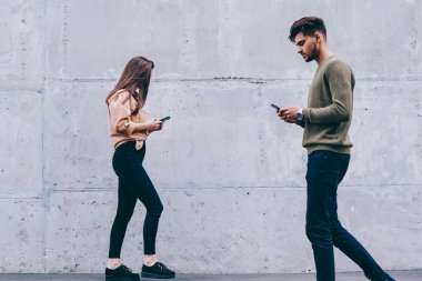 Erkek ve kadın hipsters onların akıllı telefonlar bakarak açık havada yürüyüş gerçek hayat görmezden, kız ve adam sohbet ve gadget'lar bağımlısı ağ için cep telefonu kullanarak konsantre yürüyüş