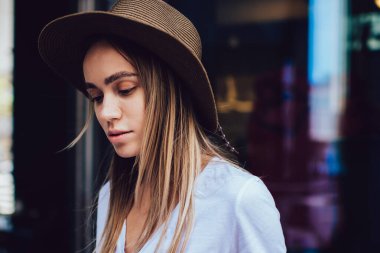 Sıradan giysiler içinde, kafenin cam duvarının yanında dikilirken dikkatle kitap okuyan çekici bir kadın.