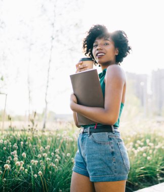 Reklam metinleri için kitabı olan çekici bir genç kızın yarım boy portresi. Doğa parkında boş zamanlarında kameraya bakıyor. Elinde kahve tutan kadının yumuşak odağı.