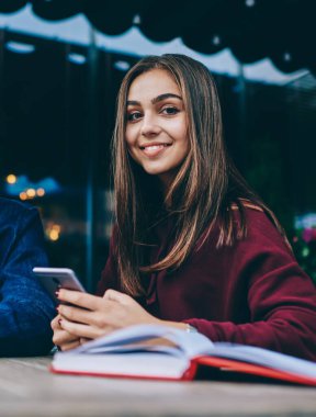 Cep telefonu kullanarak kameraya bakan genç kadın, netbook'ta görme koruması için gözlüklü erkek arkadaşı, kafe terasında teknoloji ve wifi kullanmayı öğrenen genç gençler