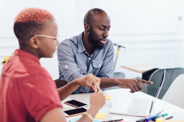 Ciddi zeki Afro-Amerikan modern iş arkadaşları dizüstü bilgisayarda geziniyor. İşaretleyicilerle masaya oturuyor. Ofisteki cep telefonlarına etiket yapıştırıyor.