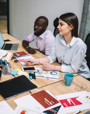 Çok ırklı genç öğrencilerin resmi kıyafet giyip bürodaki cihazları ve kırtasiyeleri kullanarak birbirlerine belgeleri açıklamalarından.