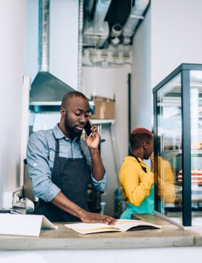 Afro-Amerikalı bir adam, hamur işi kafede çalışırken cep telefonuyla sohbet ediyor. Masanın arkasında elinde not defteriyle zenci bir kadın duruyor.