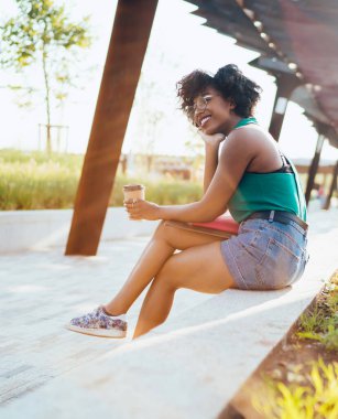Kaygısız hippi kız elinde latte içeceği ile doğada dinleniyor rüya zamanının tadını çıkarıyor şehir parkında oturan neşeli kız, yumuşak odaklı