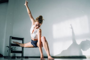 Esnek kadın plie pozisyonunda geriliyor. Sağ bacağı barre ve el kaldırıyor. Gündüz vakti parlak stüdyoda.