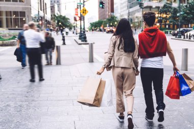 Modern şehir arka planında alışveriş torbalarıyla el ele tutuşan şık kadın ve erkeğin arka plan görüntüsü.