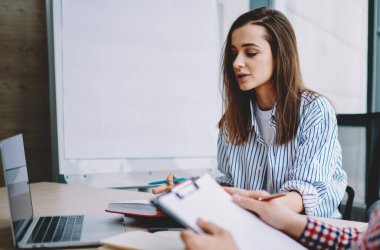 Erkek ve kadın iş ortakları gündelik giysiler içinde masa başında otururken ve modern ofiste belgeleri okurken iş teklifinde birlikte çalışıyorlar.