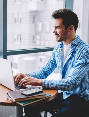 Kendine güveni olan, rahat giyinen, serbest çalışan modern dizüstü bilgisayarlı, çalışma masasında oturan bir adamdan.