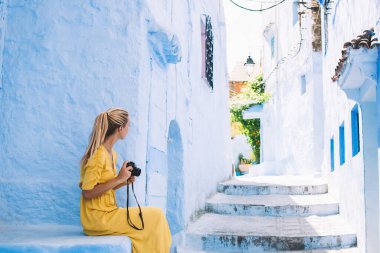 Rastgele bacak bacak üstüne atmış, Fas 'ta taş merdivenlerde oturan kamera kullanan sarışının yan görüntüsü