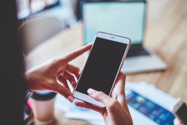 Yüzü olmayan bir çalışanın ahşap masada oturmuş akıllı telefon izlemesi, dizüstü bilgisayarlı kahve fincanı ve yaratıcı iş yerinde çalışan bir meslektaşın şemaları.