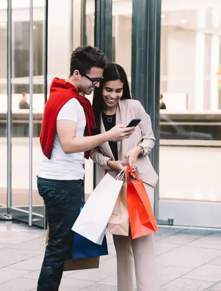 Alışveriş yaptıktan ve akıllı telefondan video izledikten sonra ellerinde kağıt torbalarla gezen mutlu ve iyimser bir çift.