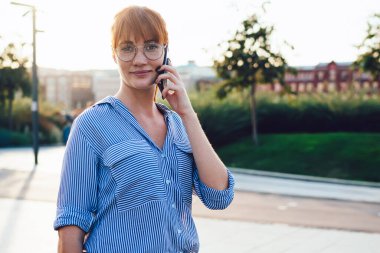 Yarım boy boyunda, rahat giyimli, gezen, beyaz tenli bir kadının cep telefonuyla konuşan hippi kız portresi. Akıllı telefon konuşmaları sokakta vergilerle tatmin oluyor.