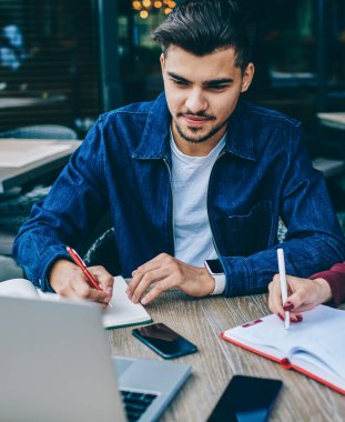 Pensive erkek ve kız öğrenciler terasta masada oturan dizüstü bilgisayarda öğretici izlerken, akıllı genç hipsters webinar bilgi notları yapma kafede wifi üzerinden netbook göz atılır