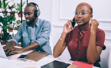 Afro-Amerikalı ciddi genç bayan iş yerinde bilgisayarını izleyen siyah bir erkekle işten dinlenerek arkadaşlarıyla iletişim kuruyor.