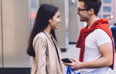 Akıllı telefonlar içinde sörf yaparken, alışveriş torbalarıyla şehir binasının yanında dikilirken ve arka planda bulanık bir şekilde birbirlerine bakarken tatlı, sevgi dolu farklı çiftlerin yan görüntüsü.