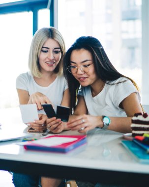 Modern neşeli kız arkadaşlar çalışma odasında masalarında oturup projeye hazırlanırken anlık fotoğraflara ve yapışkan notlara bakarlar.