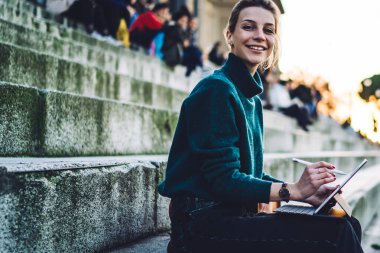 Şehrin tarihi merkezinde dinlenen elektronik stili ve taşınabilir bilgisayarı olan neşeli hipster kız portresi ve medya fotoğrafları çekmek için internet bağlantısı kullanımı, başarılı dijital göçebe