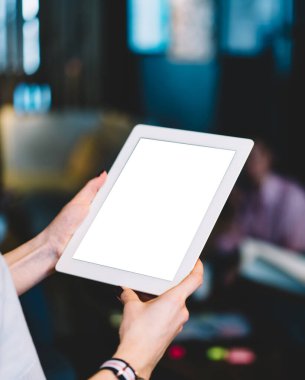 Yaratıcı iş yerindeki iş arkadaşlarının bulanık arka planında dururken boş ekran ile modern tablet üzerinde tanınamayan kadın çalışanın proje verileri taraması
