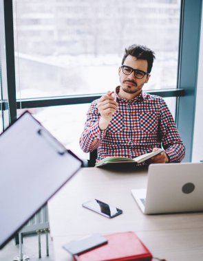 Gözlüklü, hayal kırıklığına uğramış genç bir erkek çalışanın iş arkadaşına başarısız bir proje için fırça çekerken aynı zamanda açık ofiste oturması.