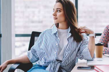 Güzel siyah saçlı bayan öğrenci sandalyede oturmuş erkek sınıf arkadaşıyla ders çalışırken dinleniyor ve modern sınıfa bakıyor.