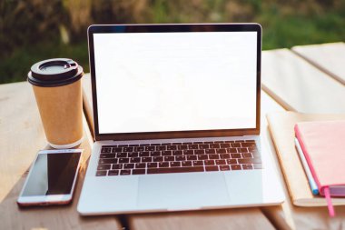 Kahve fincanı, dizüstü bilgisayar ve akıllı telefonu alıp götürün ahşap masaüzerinde açık havada duran boş kopya alanı ekranı ile dizüstü bilgisayarı açın. Temiz havada serbest işyeri. Dijital Göçebe masaüstü