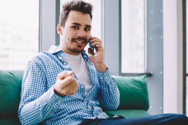 İş yerinde oturup kameraya bakarak başarıyı kutlayan iş arkadaşıyla telefon görüşmeleri yaparak sıradan giyinmiş, şaşırmış bir adam.
