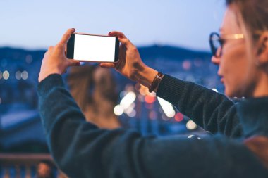 Bin yıllık hippi bir kızın günlük kıyafetleriyle, akıllı telefon uygulaması ile fotokopi ekranı ile şehir merkezini cep telefonuyla fotoğraflayan kadın turistin arka plan görüntüsü.