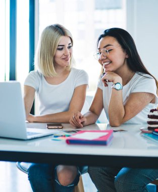 Sıradan giyinmiş, gözlüklü, neşeli, neşeli, iyimser sarışınla sohbet etmek için dizüstü bilgisayar kullanan, fırında oturmuş etkin ve zeki bir kadın.