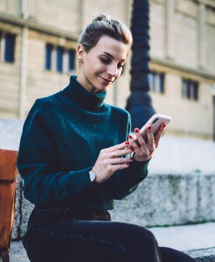 Sokak merdivenlerinde oturan, deri deri deri çantalı, eski binanın arka planında gezen, günlük kıyafetli genç bir kadından.