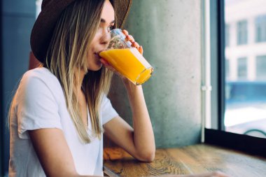 Modern kafenin penceresinin yanında duran şapkalı güzel bir kadın ve camında organik portakal suyu olan bir kadın rüya gibi gözlerini kaçırıyor.