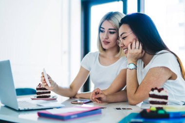 Gündüz vakti iyi aydınlatılmış çalışma odasında ödev hazırlarken çıkartma notundan bilgi okuyan gündelik genç kız arkadaşlar.