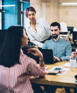 Coşkulu, zeki, çok ırklı öğrenciler kitapları kontrol ediyor, bilgisayardaki ve bilgisayardaki bilgileri incelerken geniş bir odada, ahşap masada.
