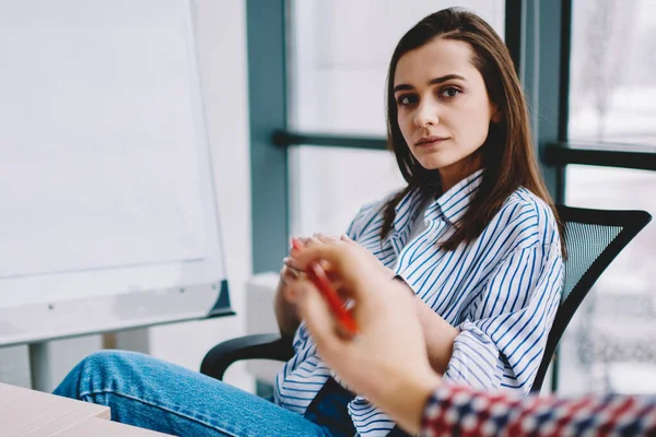 Thoughtful young attractive woman in casual clothes attentively listening colleague explaining business information while sitting and working together in light office