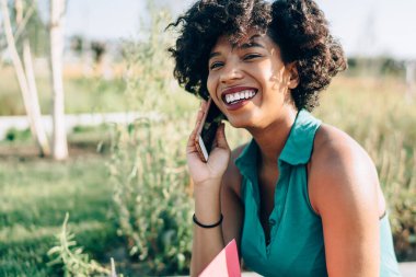Güneşli bir günde parkta akıllı telefon konuşması yapan mutlu kız öğrenci. Kaygısız hippi kız uluslararası arama için telefon cihazıyla gezinti bağlantısını kullanıyor.