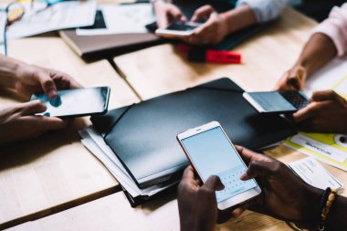 Yukarıdan tanınmayan çok ırklı girişim grubunun iş yerinde proje üzerinde çalışırken modern cep telefonlarıyla sohbet etmesi
