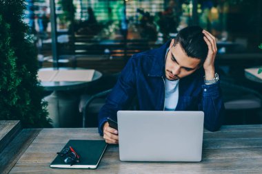 Kafe iç dizüstü bilgisayar ile oturan Pensive hipster adam bluetooth bağlantısı üzerinden multimedya paylaşmak, netbook ve kablosuz internet kullanarak serbest çalışan kafkas bin yıllık adam