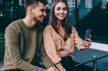 Cep telefonuyla kameraya bakan pozitif kadın dışarıda erkek arkadaşıyla fotoğraf çeken, boş zamanlarında mutlu olan romantik çift akıllı telefon kamerasıyla selfie çekiyor.