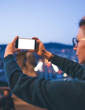 Bin yıllık hippi bir kızın günlük kıyafetleriyle, akıllı telefon uygulaması ile fotokopi ekranı ile şehir merkezini cep telefonuyla fotoğraflayan kadın turistin arka plan görüntüsü.