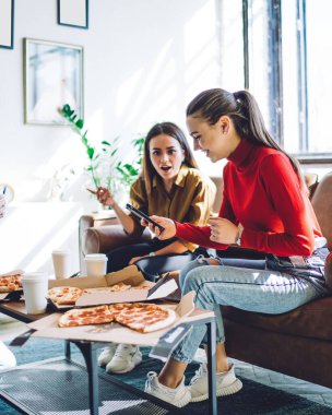 Keyifli bir kadın akıllı telefonlara göz gezdirirken gülümseyen insanlar pizza yerken ve şık bir dairede masa masa masa otururken.