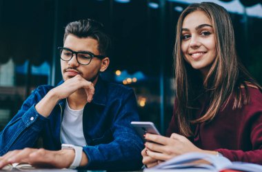 Cep telefonu kullanarak kameraya bakan genç kadın, netbook'ta görme koruması için gözlüklü erkek arkadaşı, kafe terasında teknoloji ve wifi kullanmayı öğrenen genç gençler