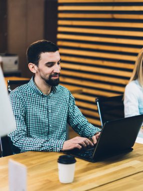 Neşeli çalışkan erkek ve kadın, odasındaki ahşap masada dizüstü bilgisayara ve modern bilgisayara yoğunlaşmışlar.