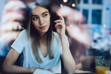 Şapkalı güzel bir kadın kafenin önünde oturmuş kitap okuyup başka tarafa bakarken taze meyve suyunun tadını çıkarıyor.