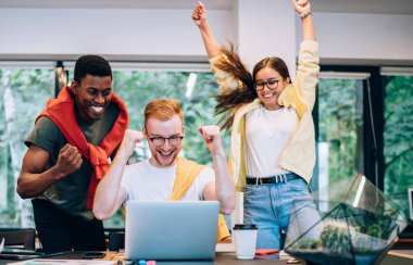 Yumruklarını sıkan ve modern yaratıcı çalışma alanında birlikte çalışırken başarılı proje başarısını kutlayan heyecanlı gençlerden oluşan bir grup.