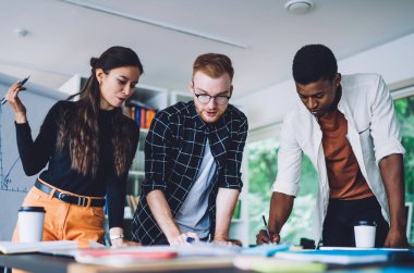 Çağdaş çalışma ortamında yaratıcı proje üzerinde çalışırken çok ırklı gençler taslak çiziyor ve birbirleriyle konuşuyorlar.