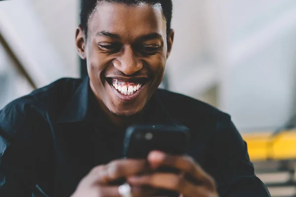 Cheerful excited black man reading positive news in social network using 4g connection on modern cellphone, happy dark skinned male watching funny comedy content via application on smartphone