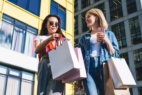 Modern şehir geçmişinden eve dönerken alışveriş merkezinde kağıt poşet taşıyan neşeli, kendine güvenen kız arkadaşlardan.